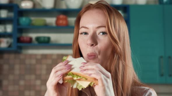 A woman in the kitchen is enjoying a sandwich