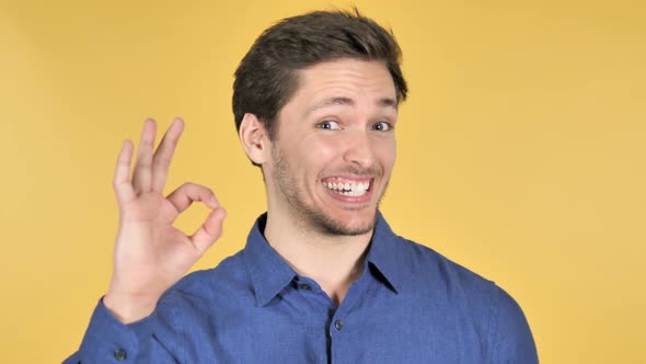 Gesture of Okay By Casual Young Man on Yellow Background