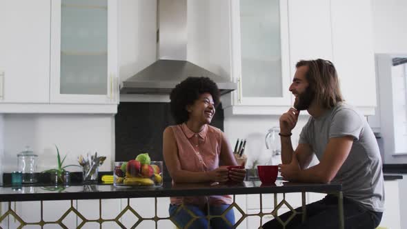 Mixed race couple holding coffee cup talking to each other in the kitchen at home