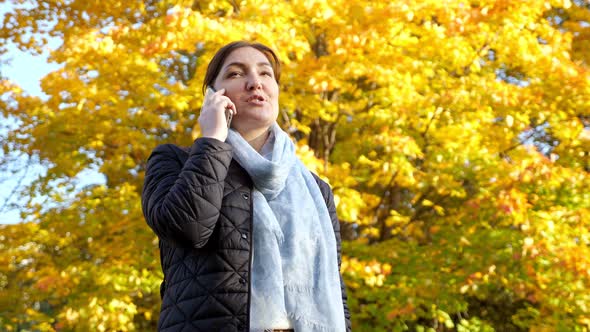 Brunette Woman Talking on the Phone Against the Background of Yellowed Trees