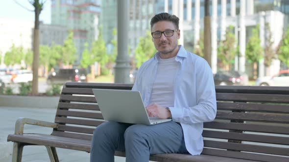 Man with Laptop Showing Thumbs Up Sign While Sitting Outdoor on Bench