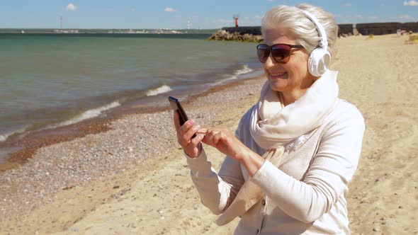 Old Woman in Headphones with Smartphone on Beach