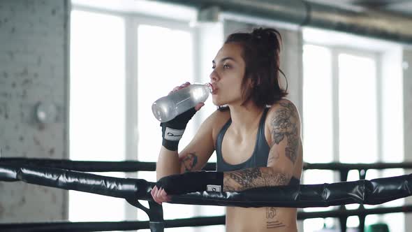 Girl Drinks Water in the Gym. Girl Resting After Workout in the Boxing Ring