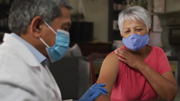 Male doctor visiting senior mixed race woman giving her vaccination