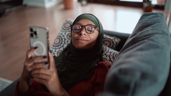 Pensive Muslim woman wearing eyeglasses texting by phone