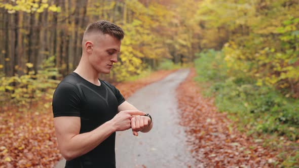 The Athlete is Standing on a Forest Road and Checking the Training Data on the Sports Watch