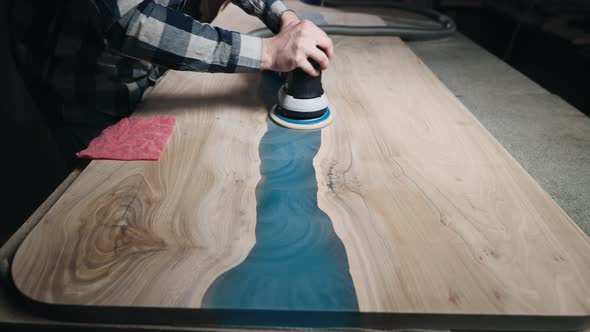 The Carpenter Processes the Surface of a Wooden Tabletop with a Grinder