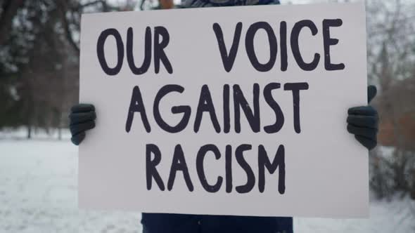 A Person is Standing with the Banner Our Voice Against Racism. Single Picket.