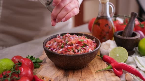 Woman Adding Pepper and Spices to Salsa Dip Sauce in Wooden Bowl at Domestic Kitchen