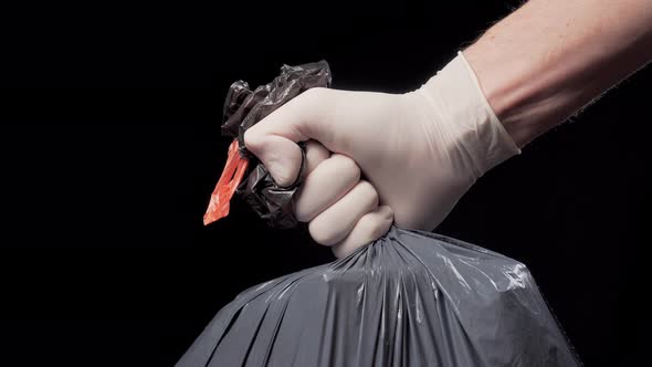 Hand in a protective glove gives a full garbage bag on a black background.