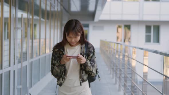 Slider Shot of Asian Teen Girl Using Smartphone Walking Outside School