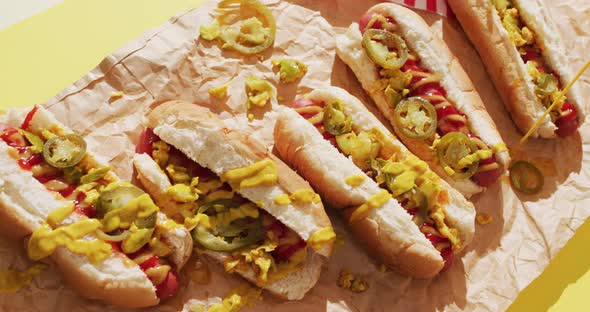 Video of hot dogs with mustard, ketchup and jalapeno on a yellow surface