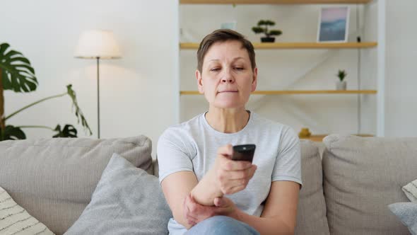Senior Lady Watching Tv in Living Room Sitting on Sofa Holding Remote Control Changing Tv Channels