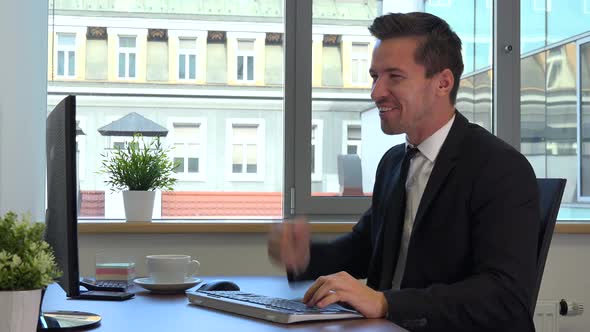 An office worker in a suit works on a computer and celebrates