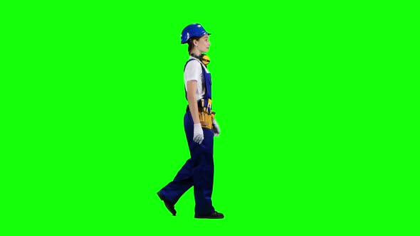 Builder Girl Is Walking Along the Street and Waving Her Hand To Others. Green Screen. Side View