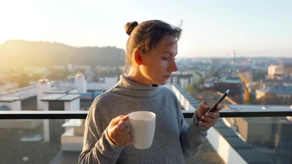 Woman Starts Her Day with a Cup of Tea or Coffee and Checking Emails in Her Smartphone on the