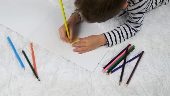 A Happy Child Draws a House with Pencils While Lying on the Floor of the House. Children's Leisure