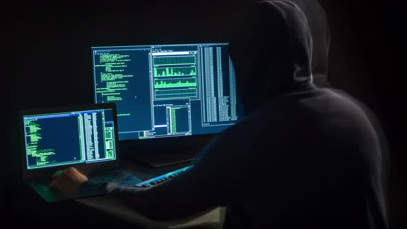 Hacker in front of two monitors with computer code