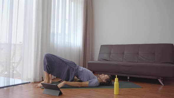 A Young Man at Home Doing Yoga Following Instructions From a Video He Watches on a Tablet