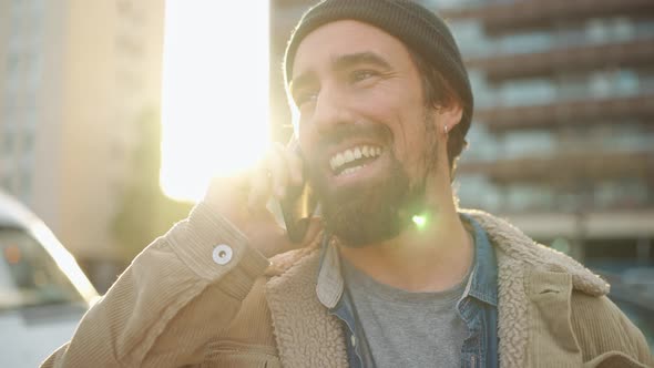 Positive bearded man wearing hat talking by phone