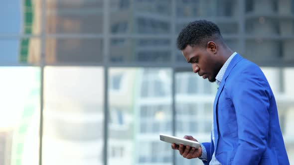 African American Man Holding White Tablet Walks in Street