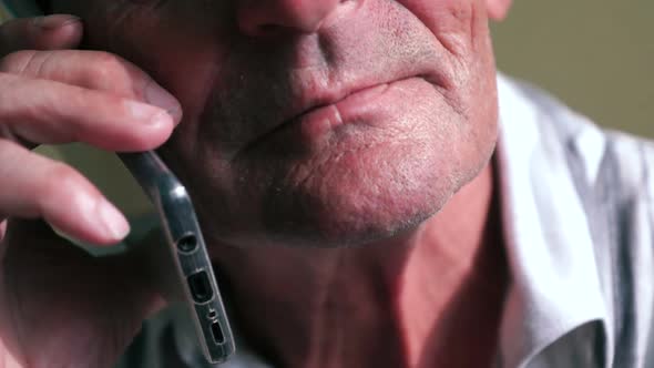 Close-up of an elderly Caucasian man listens attentively to his interlocutor while talking on a smar