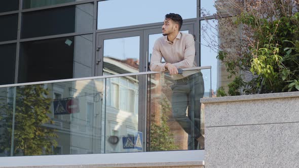 Confident Young Hispanic Business Man Standing at Railing Modern Skyscraper Office Building Looking
