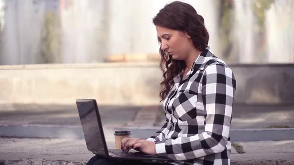 Young Attractive Girl Working on a Mobile Computer with a Serious Look Sitting on the Porch in the