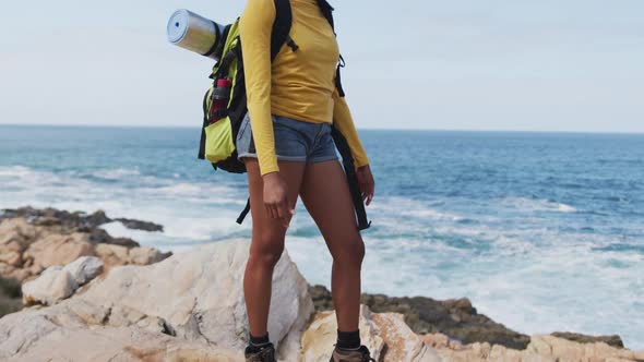 African american woman with backpack standing with her arms wide open near the ocean while hiking