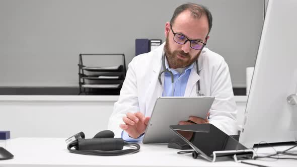 Dolly Shot of a Male Doctor with White Coat and Stethoscope Using Tablet Network Connection in