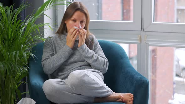 Unhealthy Woman Sits in a Chair and Sneezes or Blows Her Nose Into a Napkin Because She Has a Cold