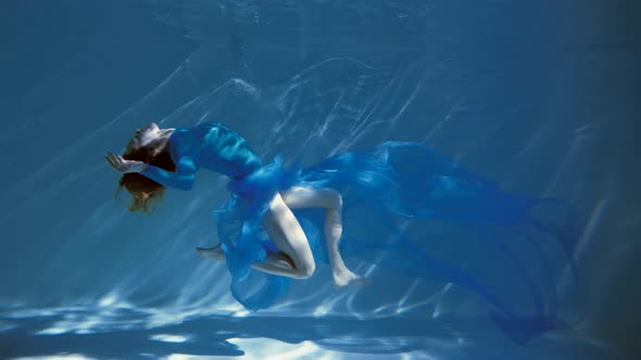 Attractive young woman swims beautifully underwater in a blue dress dress. slow motion