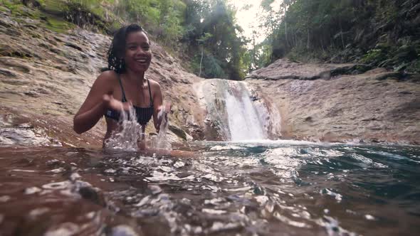 A Happy Young Woman Sits on a Stream of Water Near a Waterfall