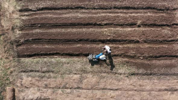 AERIAL - Man working a field with a rototiller, agriculture, wide shot zoom in