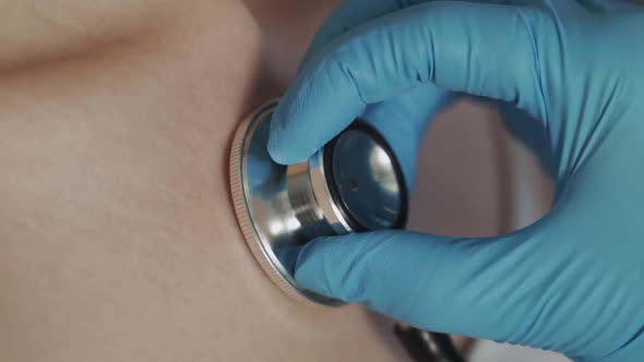 The Doctor's Hand in Medical Gloves Holds a Stethoscope and Examines the Patient