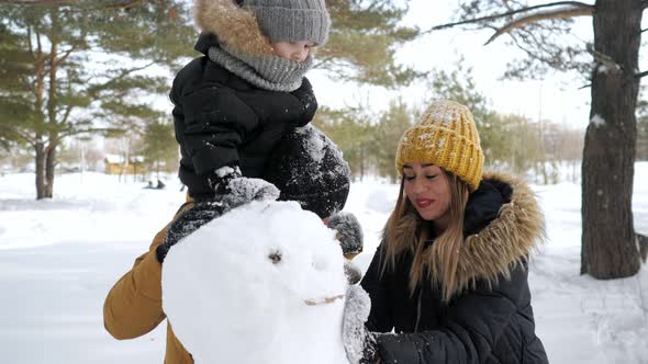 Young Family Mom Son and Dad are Building a Snowman in Winter City Park