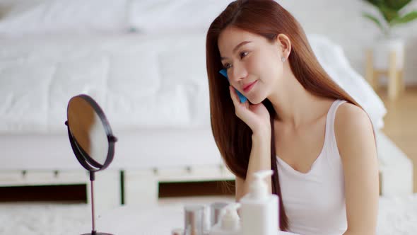 Asian young woman smile and looking in mirror doing skin care touch cheek using oil film