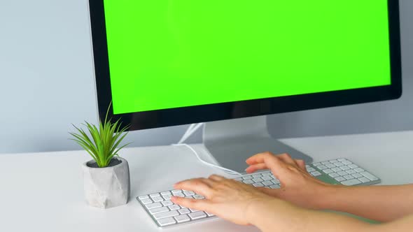 Woman Typing on a Computer Keyboard, Monitor with a Green Screen. Chroma Key. Copy Space.