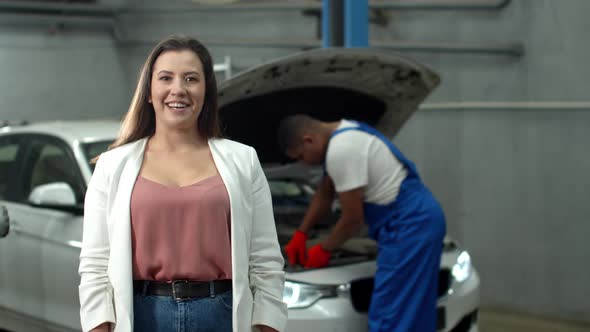 Mechanic Repairs a Car, Woman Smiles at the Camera 