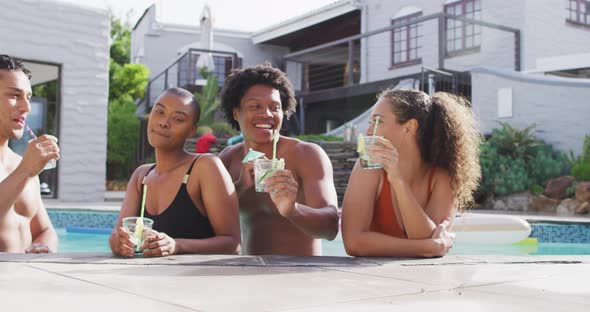 Group of diverse male and female friends with drinks laughing in swimming pool