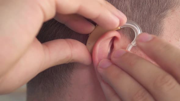 Man Inserts a Hearing Aid Into Her Ear Close Up