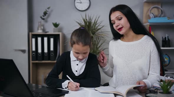 Pretty Brunette Woman which Explaining Her 10-aged Daughter How to do Hometask