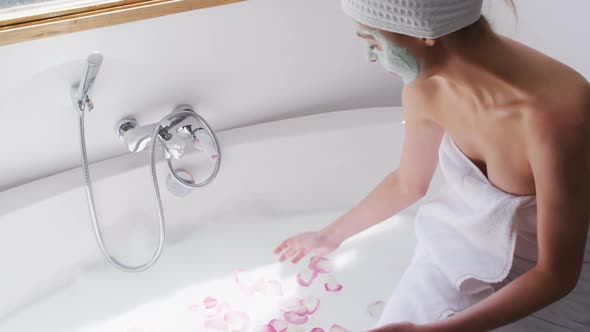 Woman wearing face pack spreading rose petals in the bathtub