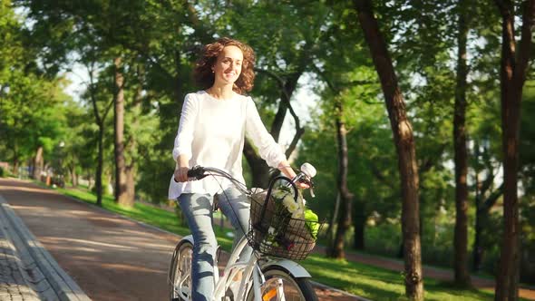 Happy Smiling Woman is Enjoying Her Time Riding a City Bicycle with a Basket and Flowers Inside