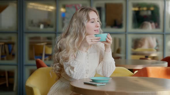 Side View of Excited Blond Woman Drinking Coffee and Waving to Unknown Friend