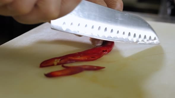 Closeup of a Gloved Chef Cutting Chili Peppers with a Knife on a Chopping Board