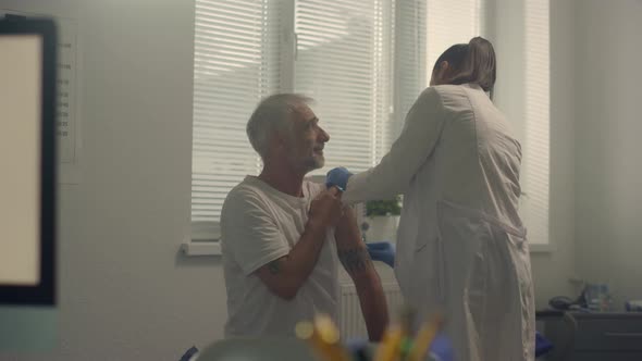 Woman Doctor Preparing Patient Shoulder to Injecting Vaccine in Modern Hospital