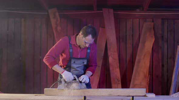 Man Carpenter in Overalls Cleans the Surface of Wooden Beam with Electric Planer