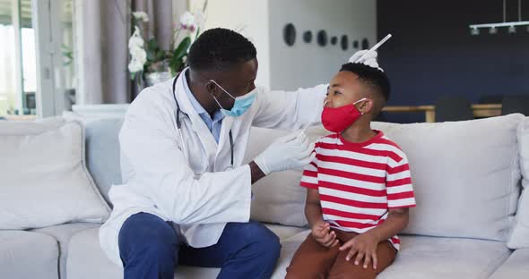 African american doctor wearing face mask taking a nasal swab sample of boy at home