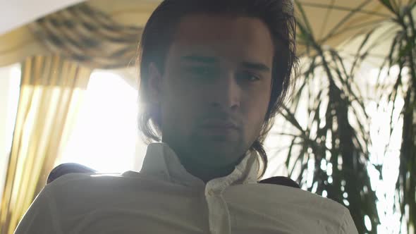 Young Handsome Man with Long Brown Hair Looking in Camera at Home